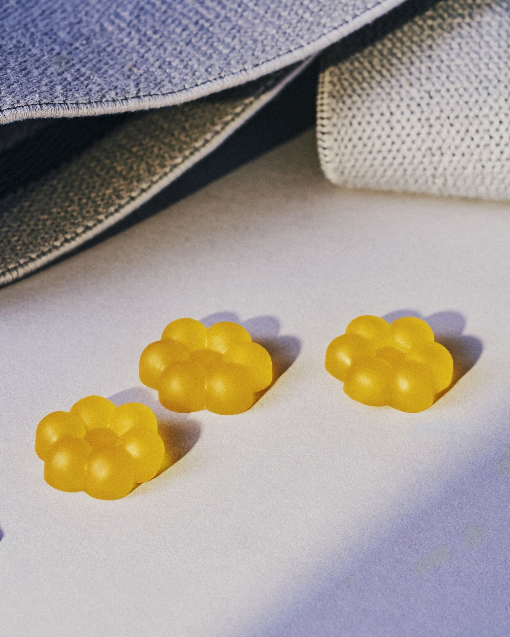 Three small translucent yellow paw-shaped accessories arranged on a light surface beside a gray textured fabric bag with white drawstrings.