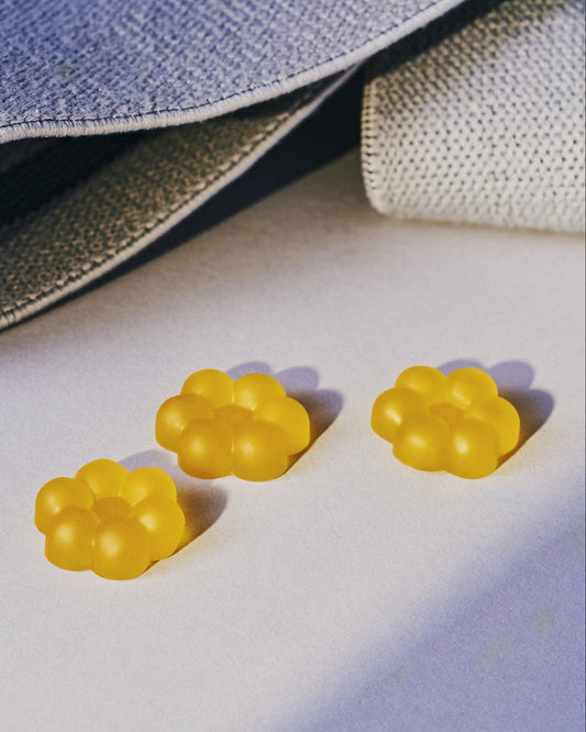 Three small translucent yellow paw-shaped accessories arranged on a light surface beside a gray textured fabric bag with white drawstrings.